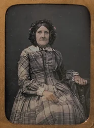 Sittande äldre kvinna i rutig klänning och huva, 1854-60.